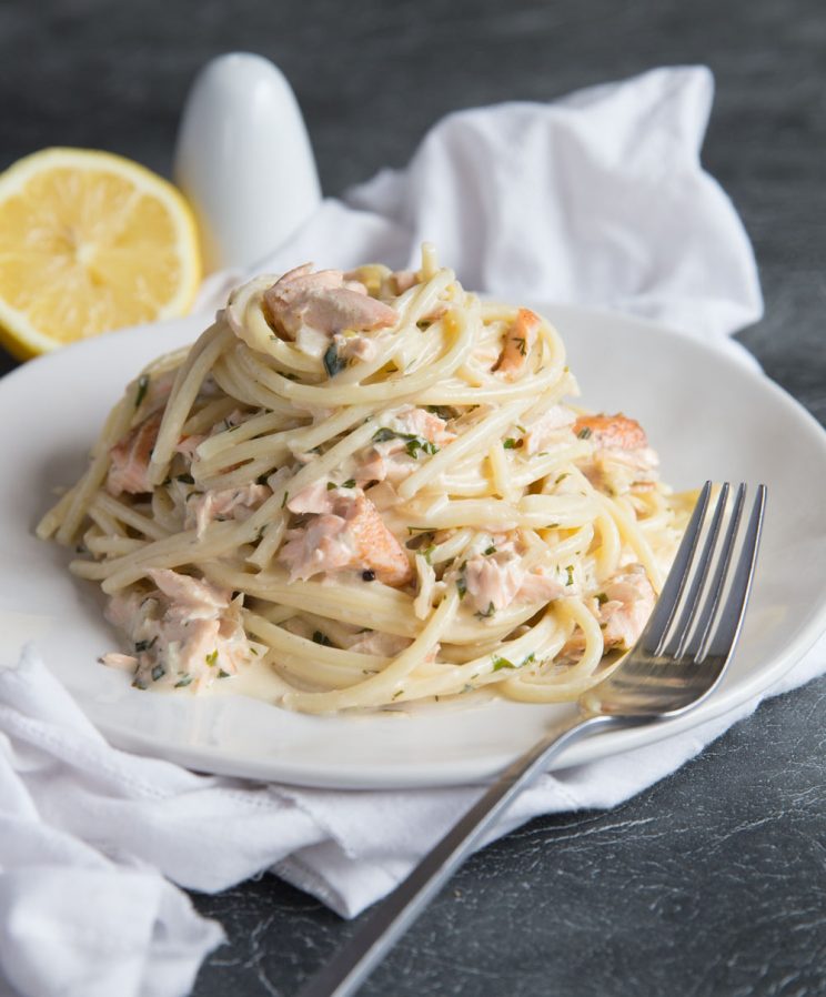 Salmon Pasta served on white plate with salt and lemon in the background